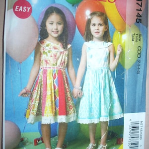 May include: A sewing pattern for two girls' dresses. The pattern is called McCall's Easy and the pattern number is M7145. The pattern is for sizes 2-3-4-5. The dresses are both sleeveless and have a Peter Pan collar. One dress is a colorful patchwork design and the other is a light blue with a geometric pattern. The girls are holding balloons.