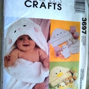 May include: A McCall's Crafts pattern envelope featuring a baby wrapped in a white hooded towel with bunny ears. The pattern includes instructions for making baby bath accessories, including a hooded towel, washcloths, and booties.