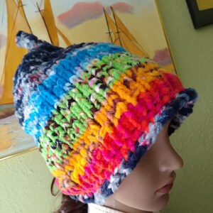 May include: A colorful knitted hat with stripes of blue, green, yellow, pink, and red. The hat has a fluffy texture and a long, pointed top.