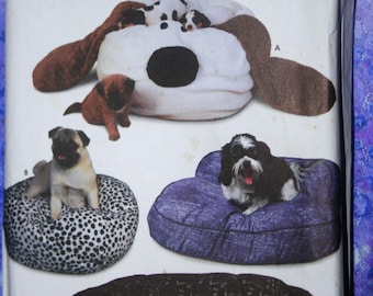 May include: A Simplicity Crafts sewing pattern for making dog beds. The pattern includes three different designs: a dog-shaped bed, a round bed with a black and white spotted fabric, and a rectangular bed with a blue fabric. The pattern also includes instructions for making the beds.