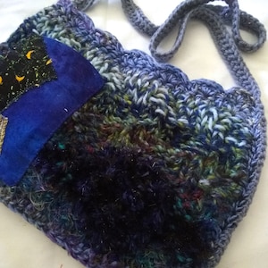 May include: A crocheted shoulder bag with a blue and green color scheme. The bag has a patchwork design with a blue fabric patch featuring a crescent moon and stars.