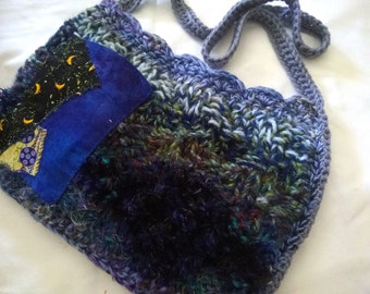 May include: A crocheted shoulder bag with a blue and green color scheme. The bag has a patchwork design with a blue fabric patch featuring a crescent moon and stars.