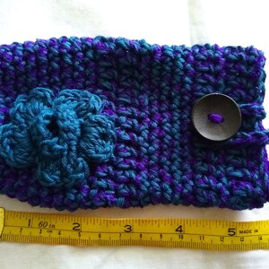May include: A crocheted purple and teal phone case with a teal flower and a black button. The case measures 6 inches long.