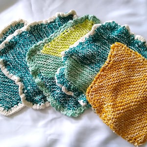 May include: A set of six knitted dishcloths in various shades of green, yellow, and white. The cloths have a scalloped edge and are made with a textured knit stitch.