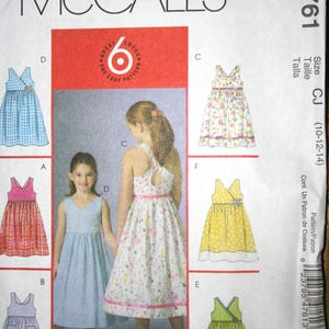 May include: McCall's sewing pattern M4761 for girls' dresses. The pattern features six different dress styles, including a gingham dress, a floral print dress, and a yellow polka dot dress. The pattern size is CJ (10-12-14).