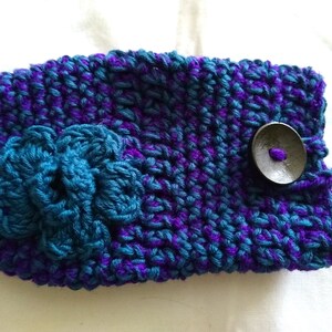 May include: A purple and teal crocheted phone case with a flower design and a black button.