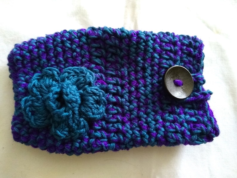 May include: A purple and teal crocheted phone case with a flower design and a black button.