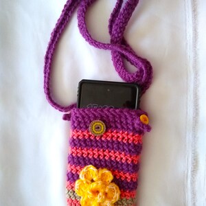 May include: Purple crocheted phone case with a yellow flower and a striped design. The case has a purple strap.