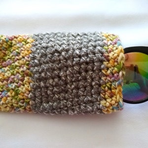 May include: A gray crocheted eyeglass case with a colorful crocheted border. The case is open and a pair of black sunglasses with iridescent lenses are partially inside.