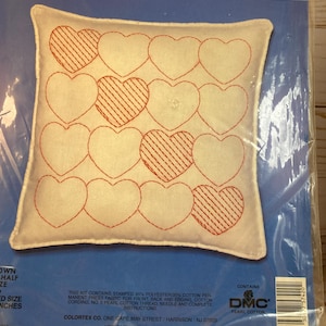 May include: A white pillow with red heart designs stitched on it. The pillow is packaged in a clear plastic bag with a label that reads "Line Stitching" and "ColorteX".