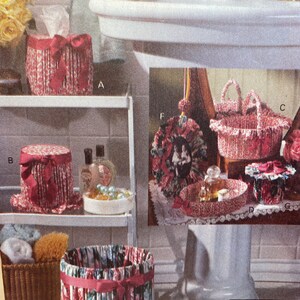 May include: A bathroom vanity with a white sink and a white pedestal. There are several fabric covered boxes and baskets in pink and red with floral patterns. The boxes are labeled with letters A, B, C, D, E, F, and G. The text "Jennie's Secret" is visible on a small sign.