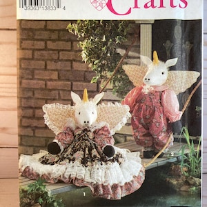 May include: Simplicity Crafts pattern number 3319, one size, for making two unicorn dolls. The dolls are dressed in pink and floral print dresses with lace trim. The dolls are holding a rope and have wings.