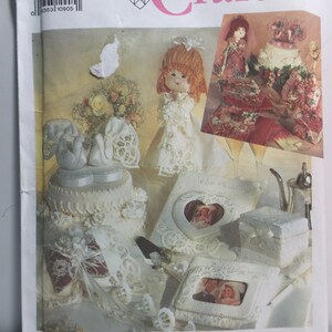 May include: A Simplicity Crafts pattern for making wedding-themed crafts. The pattern includes instructions for making a bride doll, a cake, a heart-shaped box, and a small box with a photo frame. The pattern is printed on white paper with a pink border.