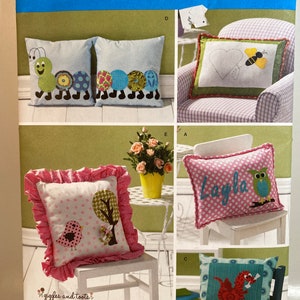 May include: A sewing pattern for making four different pillow designs. The pillows feature a variety of colorful designs, including a caterpillar, a heart with a bee, a tree with a bird, and an owl with the name "Layla".