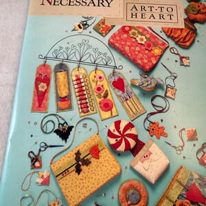 May include: A light blue craft book cover titled Sew Necessary by Art to Heart. The cover features various fabric projects including hanging banners, small pouches, a peppermint-patterned pincushion, and decorative ornaments with floral and seasonal motifs.