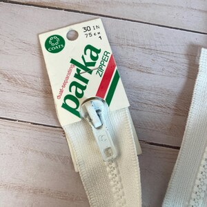 May include: White zipper with a white plastic slider. The zipper is labeled "parka zipper" and "dual-separating" on a green and red label. The label also states "30 in 75 cm 1".