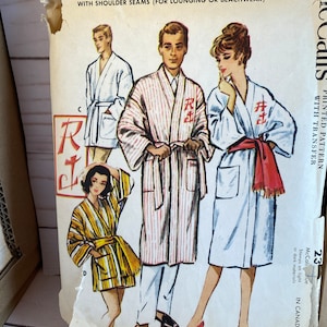 May include: Vintage sewing pattern for a men's and women's monogram robe in two lengths. The pattern includes a printed transfer for the monogram. The pattern is for sizes 23.  The pattern is printed on a white background with illustrations of three people wearing the robe.