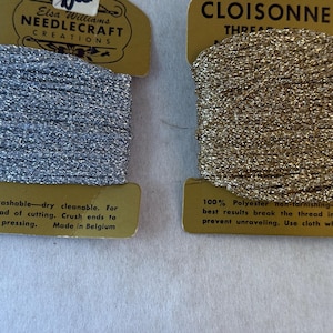 May include: Two cards of Elsa Williams Needlecraft Creations Cloisonne thread, one silver and one gold. Each card features metallic, non-tarnishing polyester thread with instructions for use printed on the bottom of the gold-colored cardboard packaging.