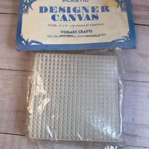 May include: A package of white plastic canvas sheets for crafting. The package is labeled "Plastic Designer Canvas" and includes the product code "PC108", size "3" x "3", and the number of sheets and holes per inch. The brand name "Vogart Crafts" and address are also printed on the package.