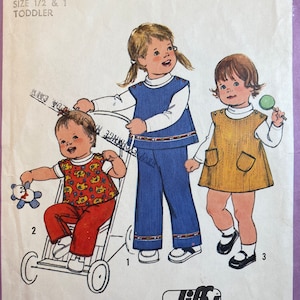 May include: Vintage children's clothing pattern featuring three toddlers in different outfits. The pattern includes a blue jumper and pants set, a red and yellow patterned shirt and pants, and a yellow jumper dress. The pattern is for sizes 1/2 and 1 toddler.