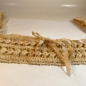 May include: A delicate crocheted lace collar with a satin ribbon tied in a bow. The collar is cream colored and the ribbon is a slightly darker shade of cream.