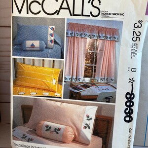 May include: A McCall's pattern envelope featuring images of bedding and curtains. The bedding includes a blue pillow with a sailboat design, a yellow pillow with sheep, and a pink pillow with rose appliques. The curtains are pink with a floral border. The text "McCall's" is at the top.