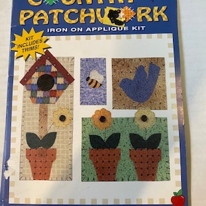 May include: A craft kit for making a country-themed patchwork design. The kit includes die-cut shapes, trims, and instructions. The design features a birdhouse, a bee, a bird, and two potted flowers. The kit is called "Growing Things" and is made in the USA.