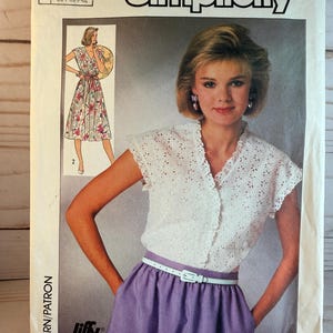 May include: Simplicity sewing pattern 7455. The pattern features a woman wearing a white eyelet top, a purple skirt, and a white belt. The pattern also shows a floral dress. The text "Jiffy" is visible.