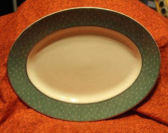 May include: An oval serving platter with a green and white polka dot design. The platter has a gold rim and is made of ceramic.