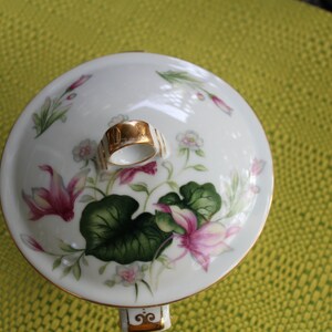 May include: White porcelain lid with a gold trim and floral design. The lid has a gold knob with a ring.