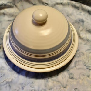 May include: A white ceramic serving dish with a blue and white striped design. The dish has a lid with a knob on top.