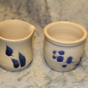 Hand thrown pottery creamer and sugar set. White decorated with blue flowers and leaves
