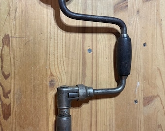 Puede incluir: Un taladro de manivela vintage con un mango de madera y una manivela de metal. El taladro está hecho de metal y tiene un acabado negro. Es una herramienta útil para perforar agujeros en la madera.