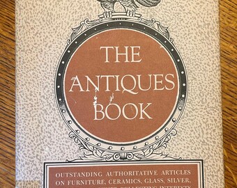 May include: The cover of a book titled "The Antiques Book" with an illustration of an eagle with outstretched wings above a circular design. The book features articles on furniture, ceramics, glass, silver, pewter, and other collecting interests. It is illustrated with photographs of over two hundred items and edited by Alice Winchester and the staff of The Magazine Antiques.