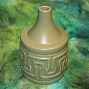 May include: A green ceramic vase with a geometric design. The vase has a wide base and a narrow neck.
