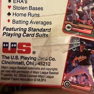 Pu&ograve; includere: Un primo piano di una scatola di carte da gioco a tema baseball. La scatola &egrave; rossa, bianca e blu con il testo "The U.S. Playing Card Co. Cincinnati, Ohio 45212" stampato sul davanti. La scatola presenta anche un logo della U.S. Playing Card Company e il testo "Featuring Standard Playing Card Suits".