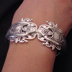 May include: A silver bracelet with an ornate design featuring a floral motif. The bracelet is made from a repurposed spoon and has a unique, handcrafted look.