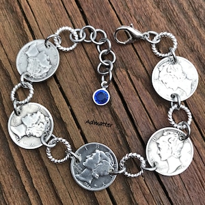 May include: A silver bracelet with five silver coins and a blue crystal charm. The coins have the profile of a woman on them and the year 1940.