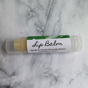 May include: A clear tube of lip balm with a white label that reads "Lip Balm" and lists the ingredients: Avocado Oil, Lanolin, Beeswax, Cocoa Butter, Vitamin E.