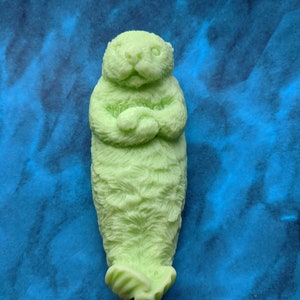 May include: A green sea otter soap sculpture with a detailed, textured surface. The otter is curled up in a sleeping position with its paws tucked under its chin.