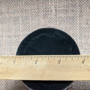 May include: A black hockey puck measuring 3 inches in diameter, resting on a burlap surface.