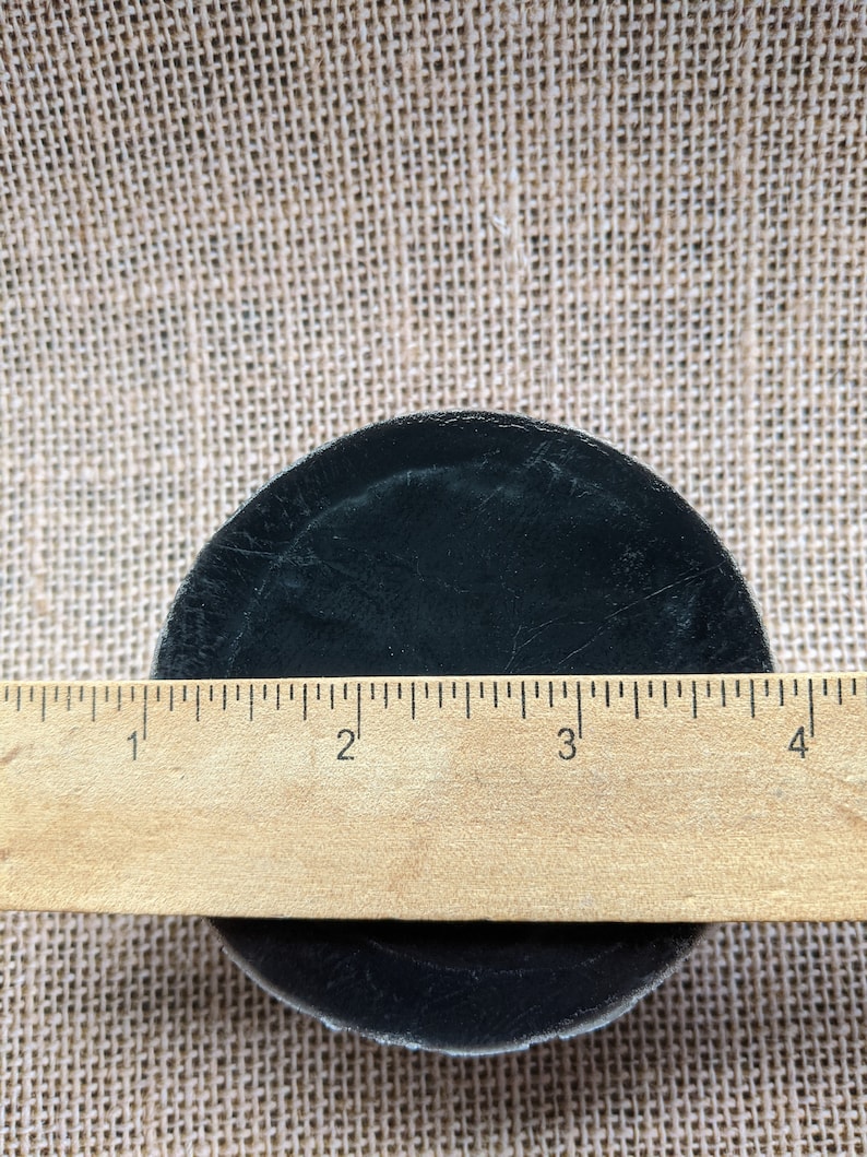 May include: A black hockey puck measuring 3 inches in diameter, resting on a burlap surface.