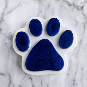 May include: A white paw print with blue resin filling the paw pads. The paw print is a decorative item.