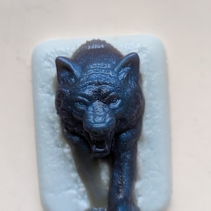 May include: A dark blue wolf figurine with a snarling expression, standing on a light blue background.