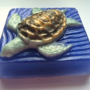 May include: A blue and green soap bar with a detailed sea turtle design. The turtle is swimming on a blue wave pattern.