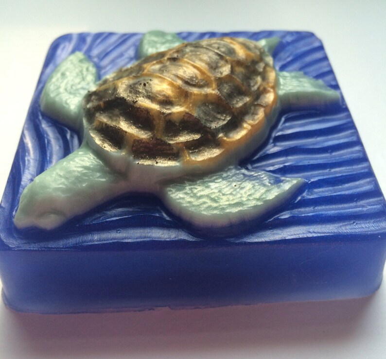 May include: A blue and green soap bar with a detailed sea turtle design. The turtle is swimming on a blue wave pattern.