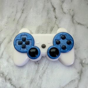 May include: A white plastic video game controller with blue buttons and black accents. The controller is on a white marble surface.