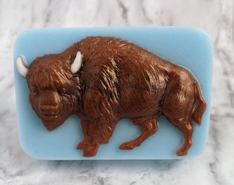 May include: A brown and white bison figurine on a light blue background. The bison is made of a shiny material and has a detailed design.