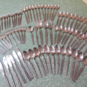 May include: A large collection of stainless steel flatware including various forks, spoons, and knives. Each piece features a textured, patterned handle design. The set contains multiple sizes of dinner forks, salad forks, teaspoons, soup spoons, and dinner knives arranged in a group.