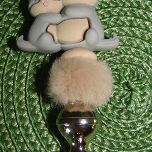 May include: A silver bottle stopper with a furry top and two gray ceramic animal figurines hugging each other.